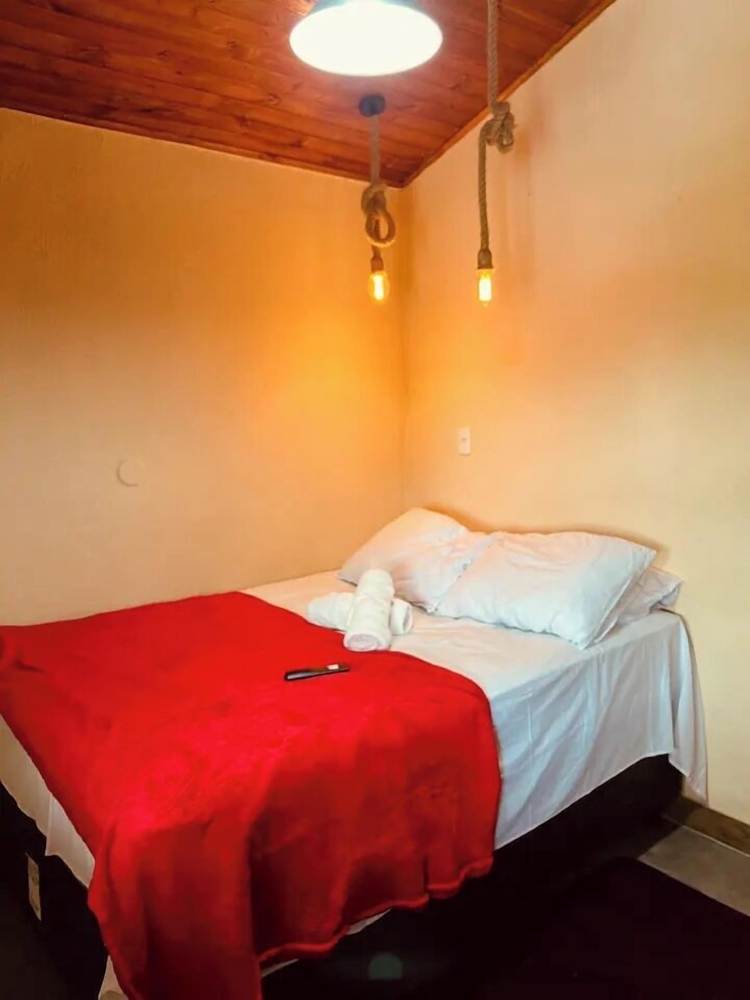 A small, single-bed room with a wooden ceiling, a red blanket, and a white pillow.