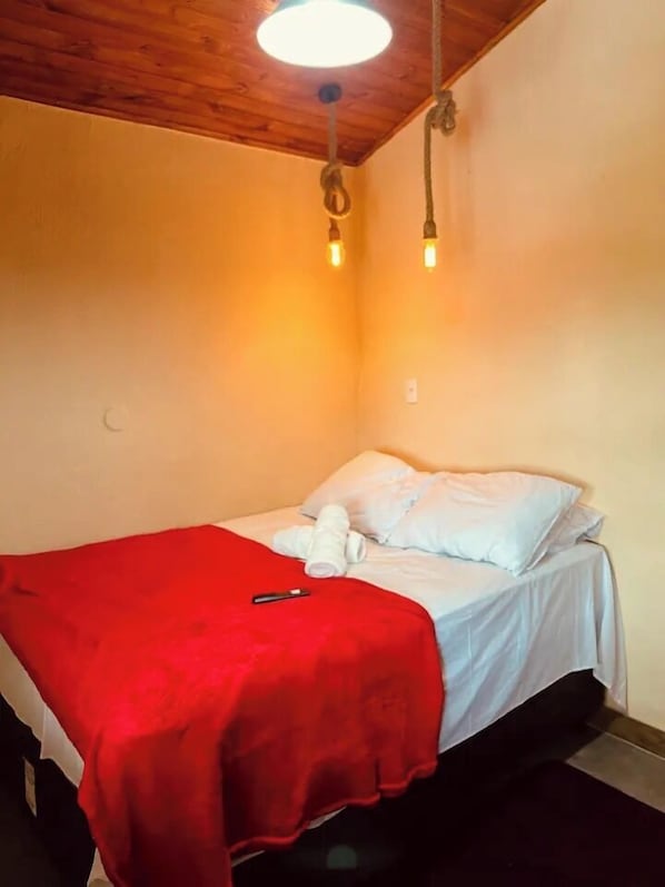 A small, single-bed room with a wooden ceiling, a red blanket, and a white pillow. - Suíte charmosa a 30 m da Orla Bardot 01 (Búzios)