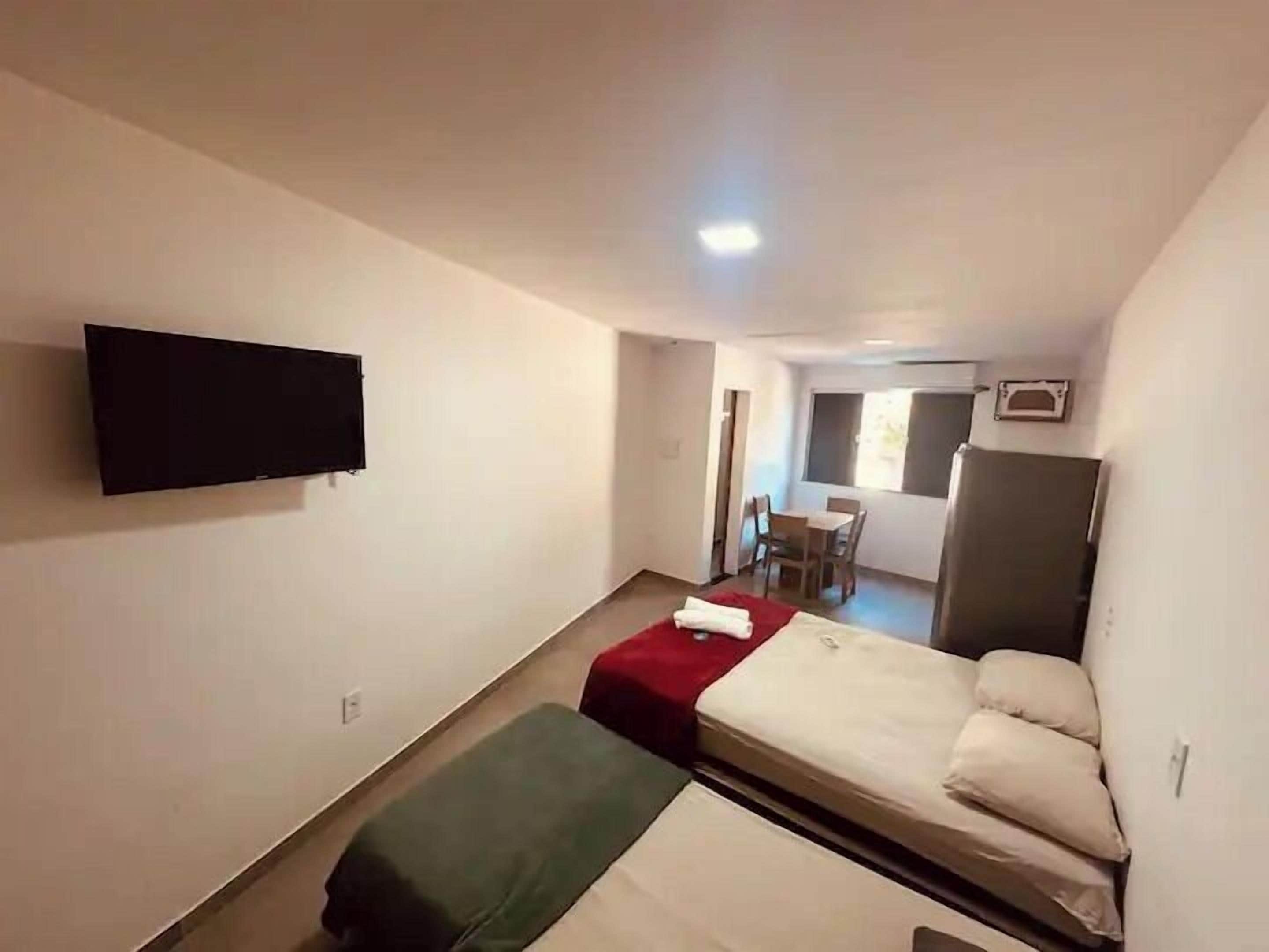 A compact hotel room with a single bed, a small desk, a chair, a television mounted on the wall, and a window providing natural light.