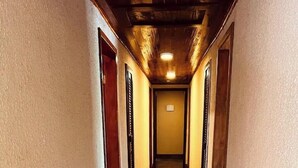 Ein schmaler, mit Holzdielen belegter Gang mit Türen an beiden Seiten, der zu einem Raum mit heller Wand und Deckenleuchte führt.