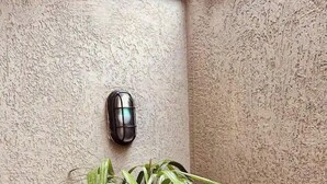 Eine Hausecke mit strukturierter Wand, einem Blumentopf, einer Wandleuchte und einem Holzpflanzgefäß mit Kies.