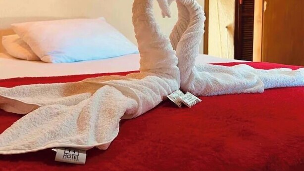 Ein Hotelzimmer mit roter Bettdecke, einem weißen Kissen und einer Handtuchgestaltung in Herzform.
