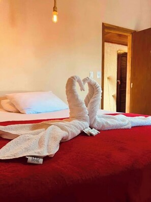 A hotel room with a red bedspread, a white pillow, and a towel artfully arranged to resemble a heart shape. - Suíte charmosa a 30 m da Orla Bardot 01 (Búzios)