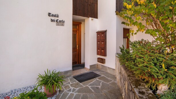 Una entrada de edificio con un letrero que dice 'Taulà dei Carli', una puerta de madera, un pequeño armario de madera y una planta en maceta.