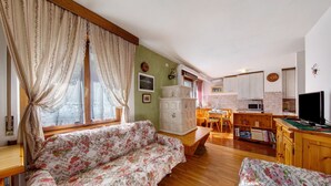 Una sala de estar acogedora con un sofá floral, suelo de madera, una zona de comedor y una cocina con armarios y televisión.