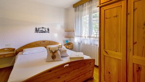 Una cama de madera con colchón blanco, un cojín con diseño de ciervo y una mesita de noche con una lámpara.