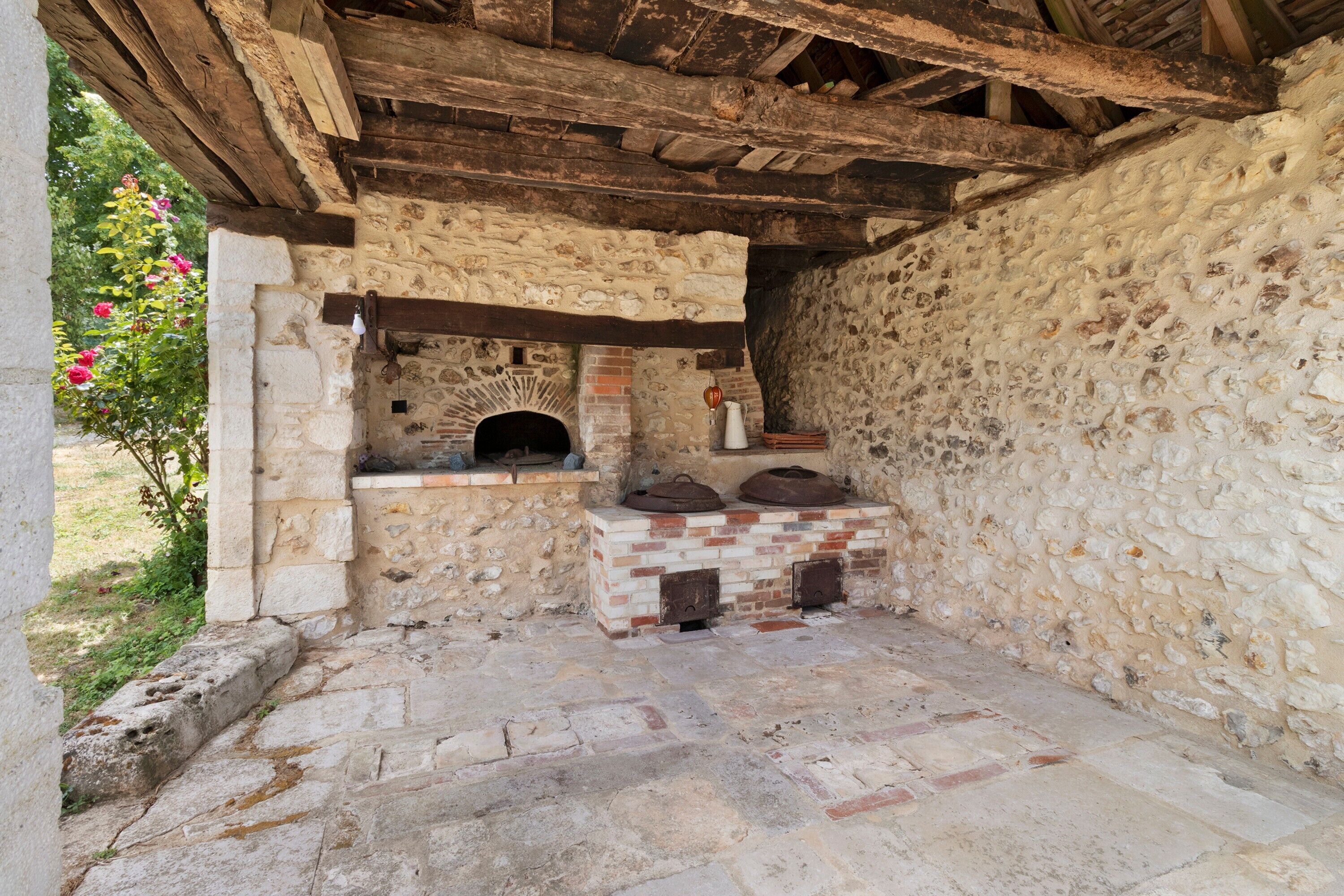 Ein Zimmer mit Steinwänden, einem Backofen aus Ziegeln, Holzbalken und einem Steinfußboden.