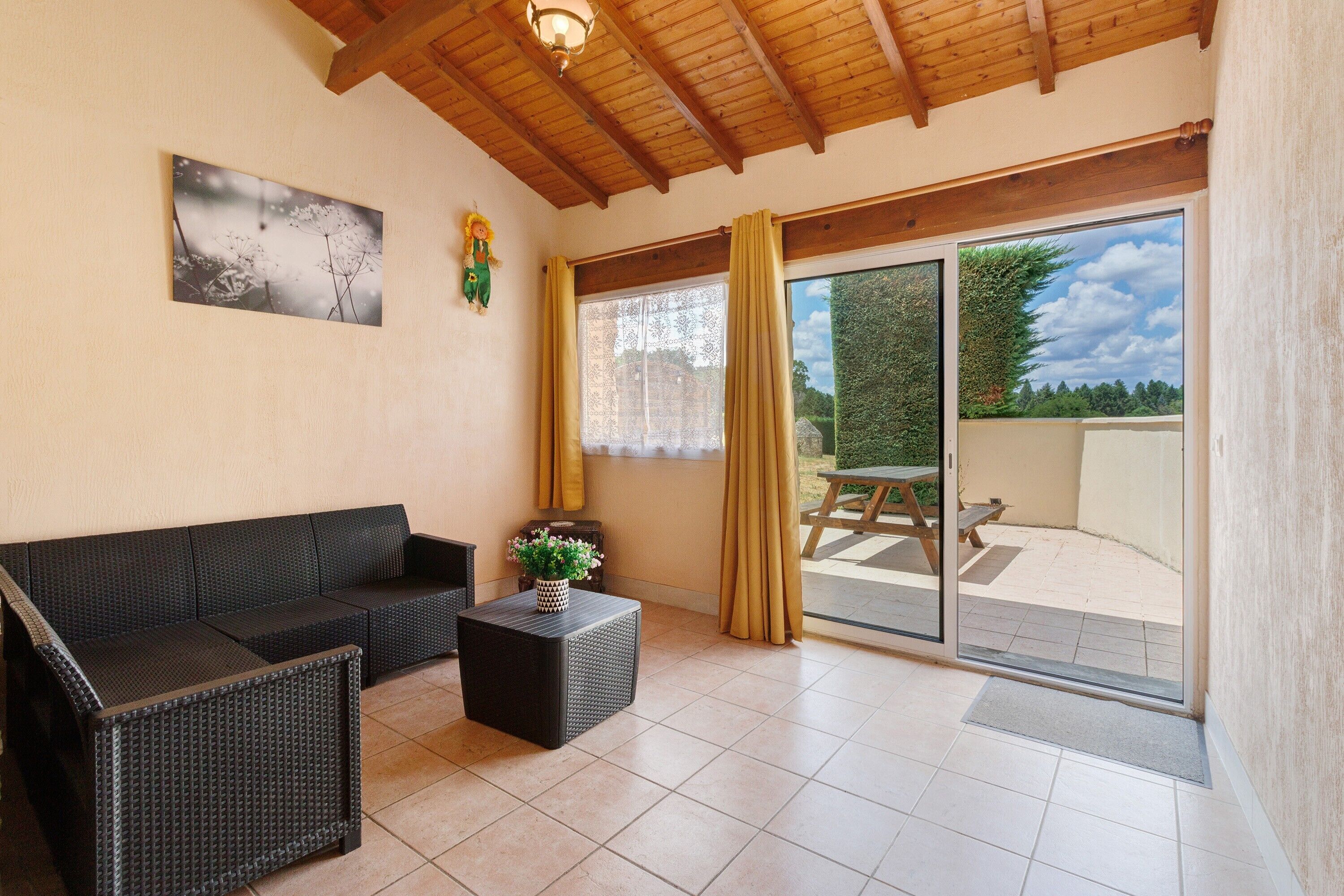 A room with a sofa, a small table with a plant, a window with curtains, and a view of an outdoor patio.