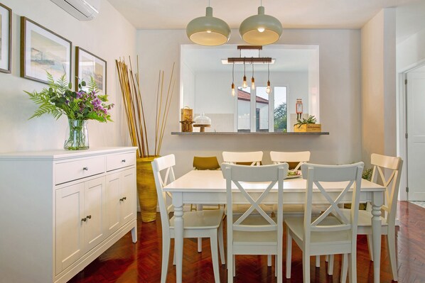 A dining area with a white table, four chairs, a vase with flowers, and a mirror above the table.