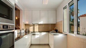 Een moderne keuken met witte kasten, een inbouwmagnetron en een raam met uitzicht op palmbomen.