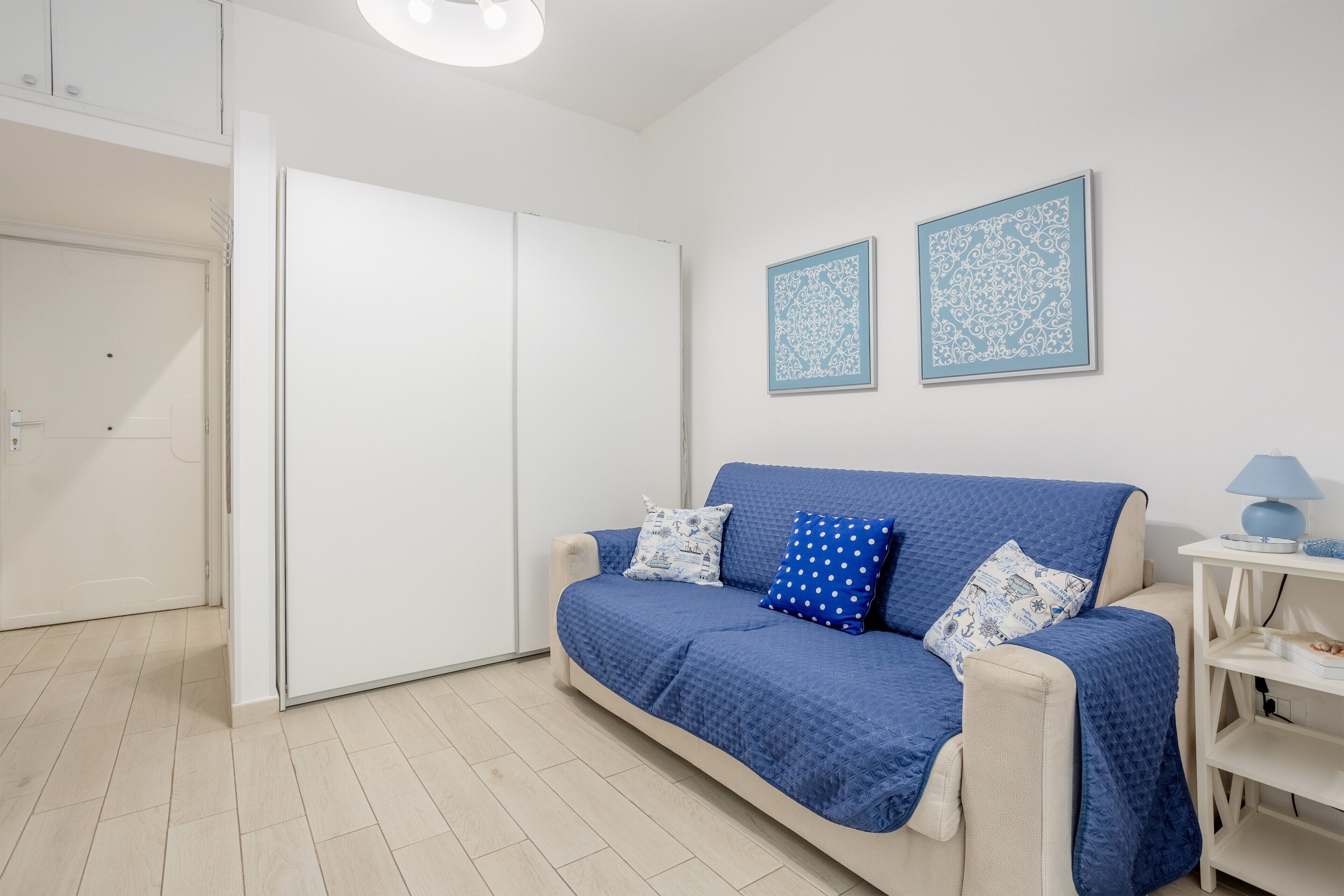 Ein Zimmer mit einem blauen Sofa, einem weißen Kleiderschrank und zwei gerahmten Wandbildern.