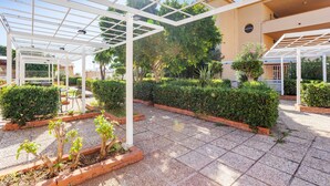 A covered outdoor area with a tiled floor, white pergola structures, and neatly trimmed hedges. - Studio 'Flat Blu Palermo Mondello' with Shared Pool, Shared Terrace & Air Conditioning (Palermo)