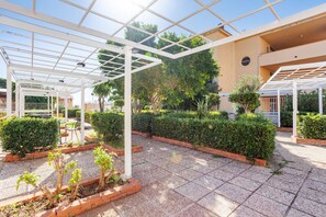 A covered outdoor area with a tiled floor, white pergola structures, and neatly trimmed hedges. - Studio 'Flat Blu Palermo Mondello' with Shared Pool, Shared Terrace, and Air Conditioning (Palermo)