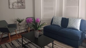 A living room with a blue sofa, two side tables, a coffee table, and a painting on the wall. - The Town-Suite at Wanskuck NEW 2-BR APT  Parking (Povidence)