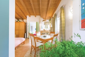 A wooden ceiling, a dining table with chairs, a bed, and a green plant.