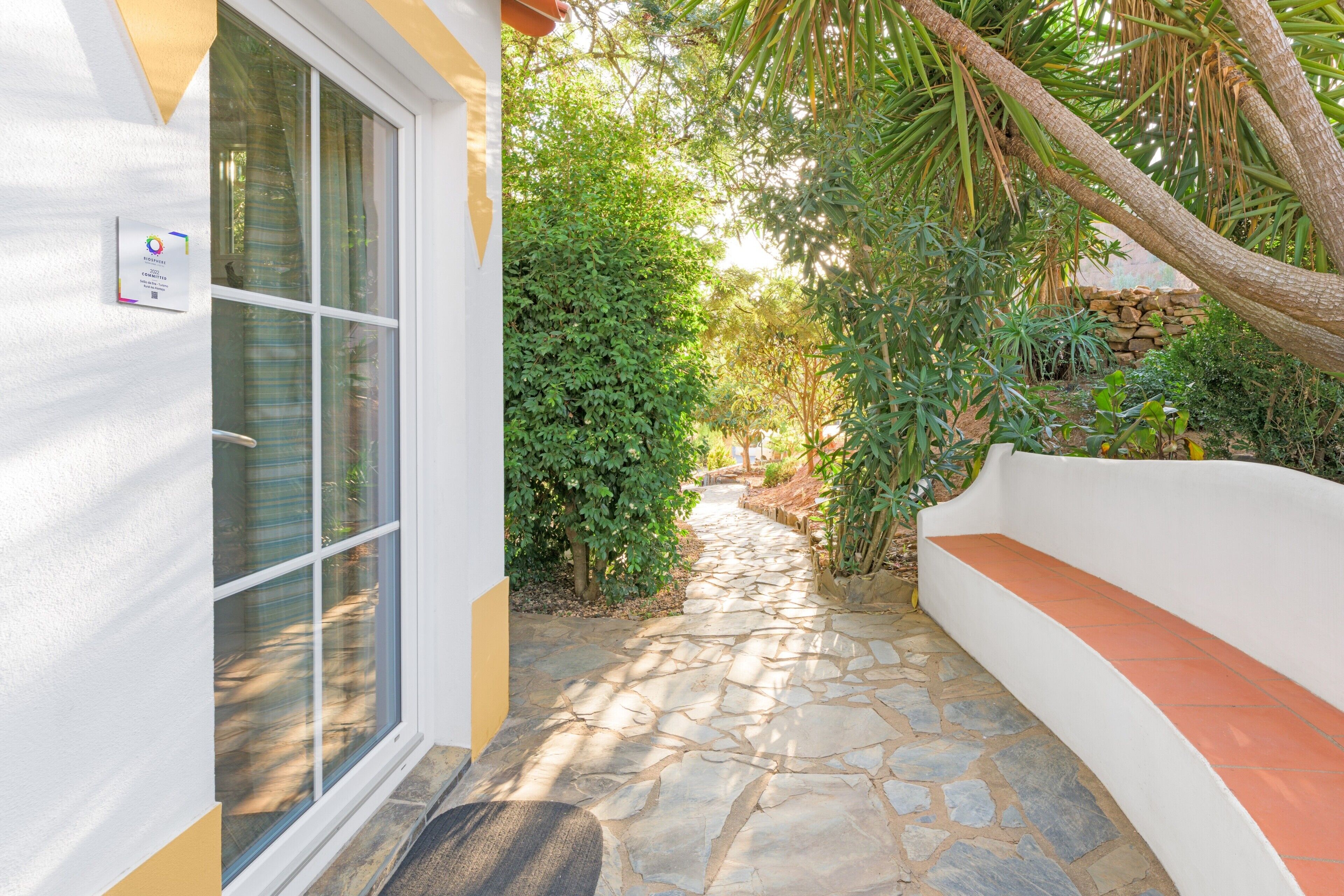 A stone pathway leading to a white building with a glass door and a bench.