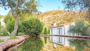 Une maison avec un toit rouge, une façade blanche et son reflet dans l’eau.