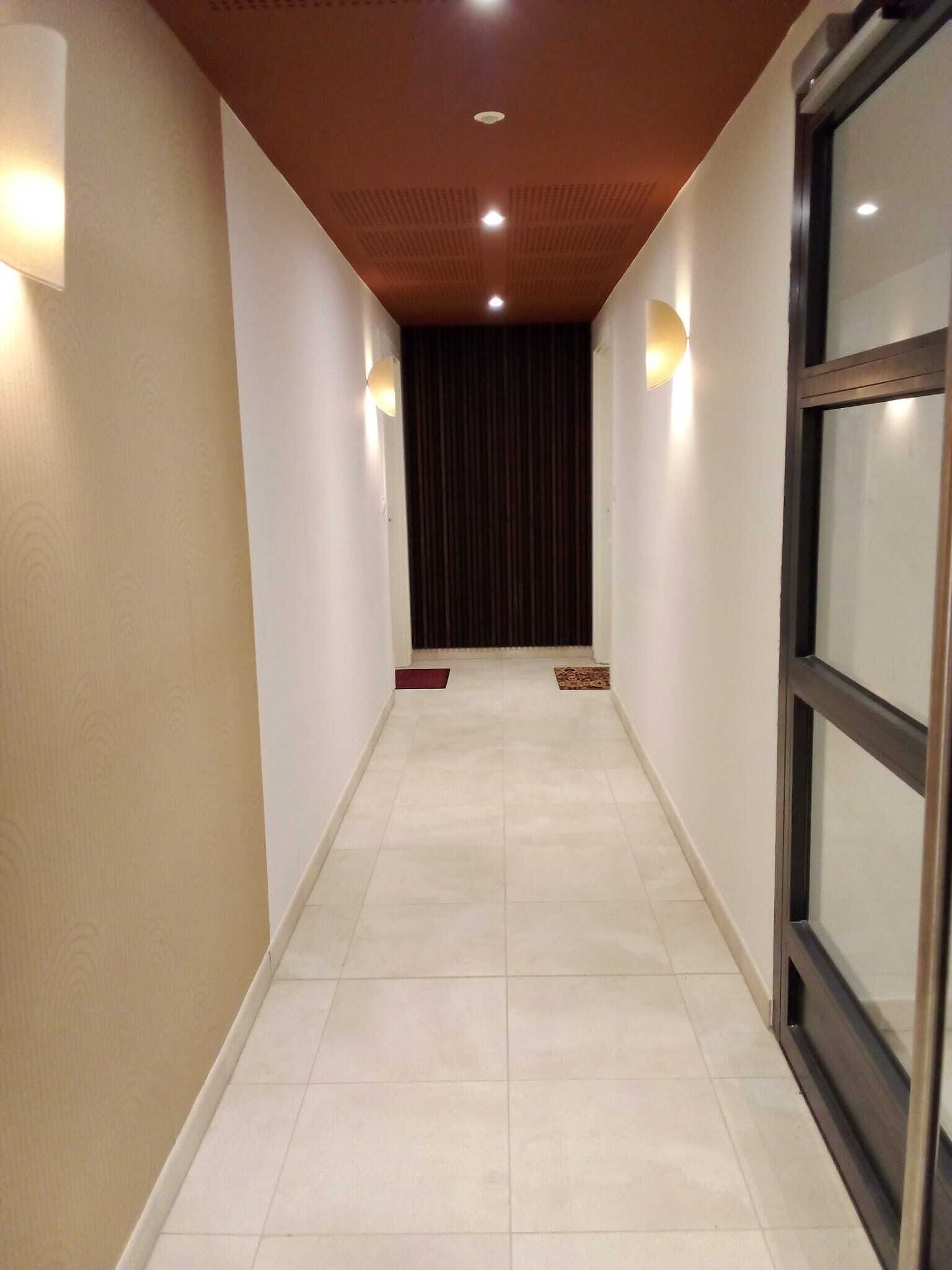 Un pasillo con suelo de baldosas, techo de madera y dos luces fijadas a la pared.