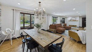 A spacious living room with a wooden dining table, black chairs, a brown sofa, and a chandelier.