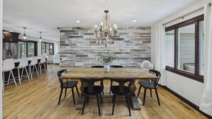 A spacious dining area with a rustic brick wall, a wooden dining table, and modern black chairs.