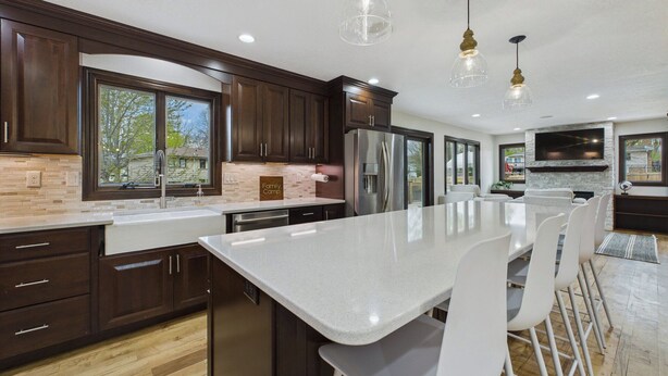 A modern kitchen with dark wood cabinets, a large island with bar stools, and pendant lighting.