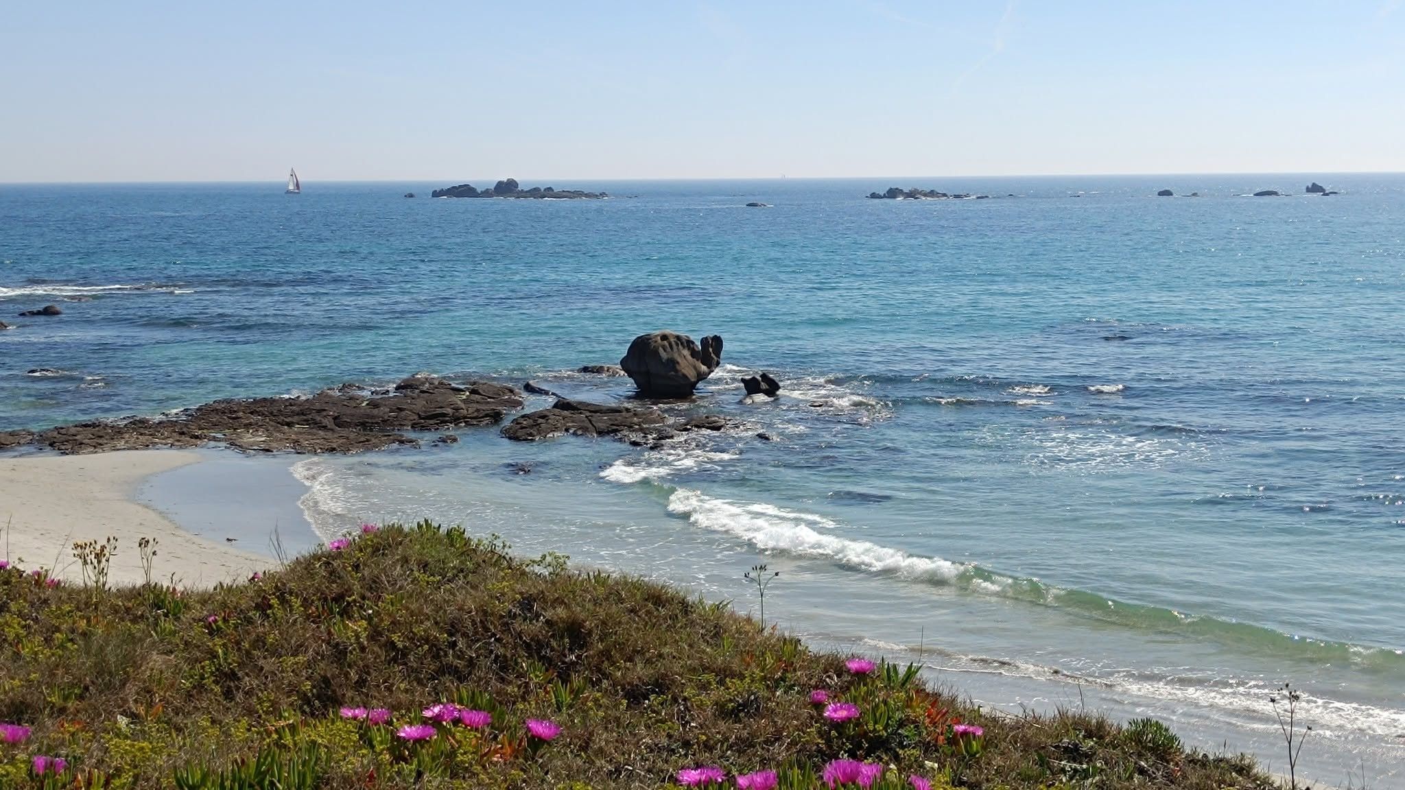 Eine Küstenlandschaft mit Felsen, klarem blauen Wasser und einem Sandstrand.