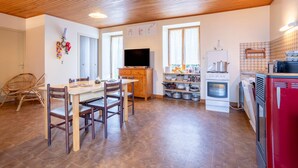 Una cocina con armarios de madera, un televisor, una mesa de comedor con sillas y un refrigerador rojo.