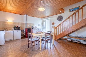 A kitchen with a dining table, chairs, a wooden staircase, and a clock on the wall.