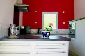 A kitchen with red walls, a window, a stove, and a blue and white bowl with flowers on the counter.