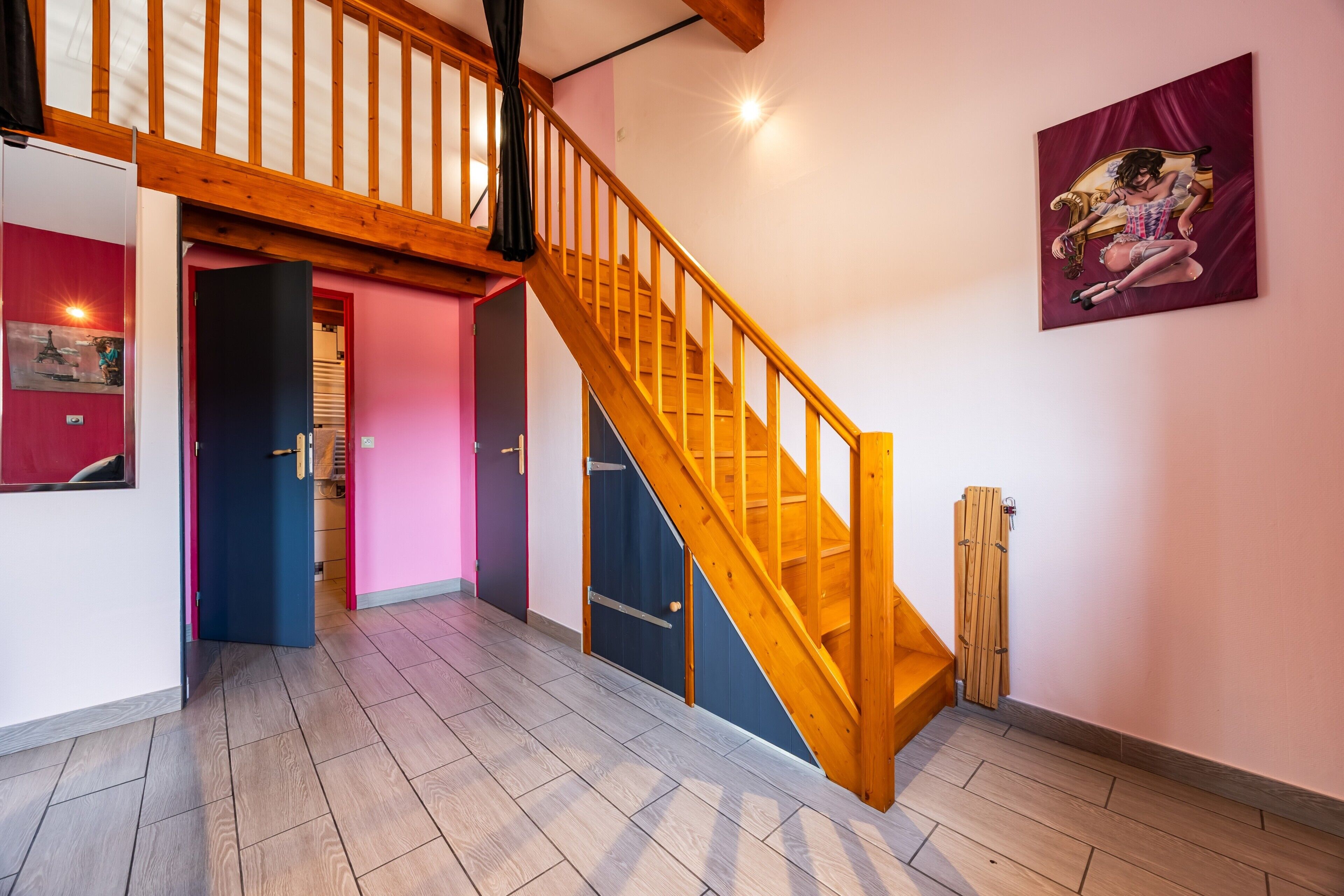 A staircase with wooden railings leading to an upper floor, a door with a black handle, and a wall-mounted artwork.