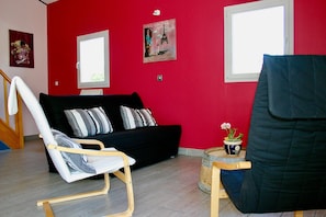 A room with a red wall, a black sofa with striped pillows, a white chair, and a small table with a potted plant.
