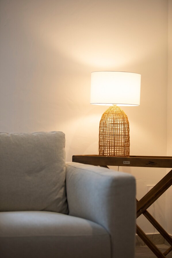 Une chambre moderne avec un canapé blanc, une table d’appoint en bois et une lampe originale en fibres tressées.