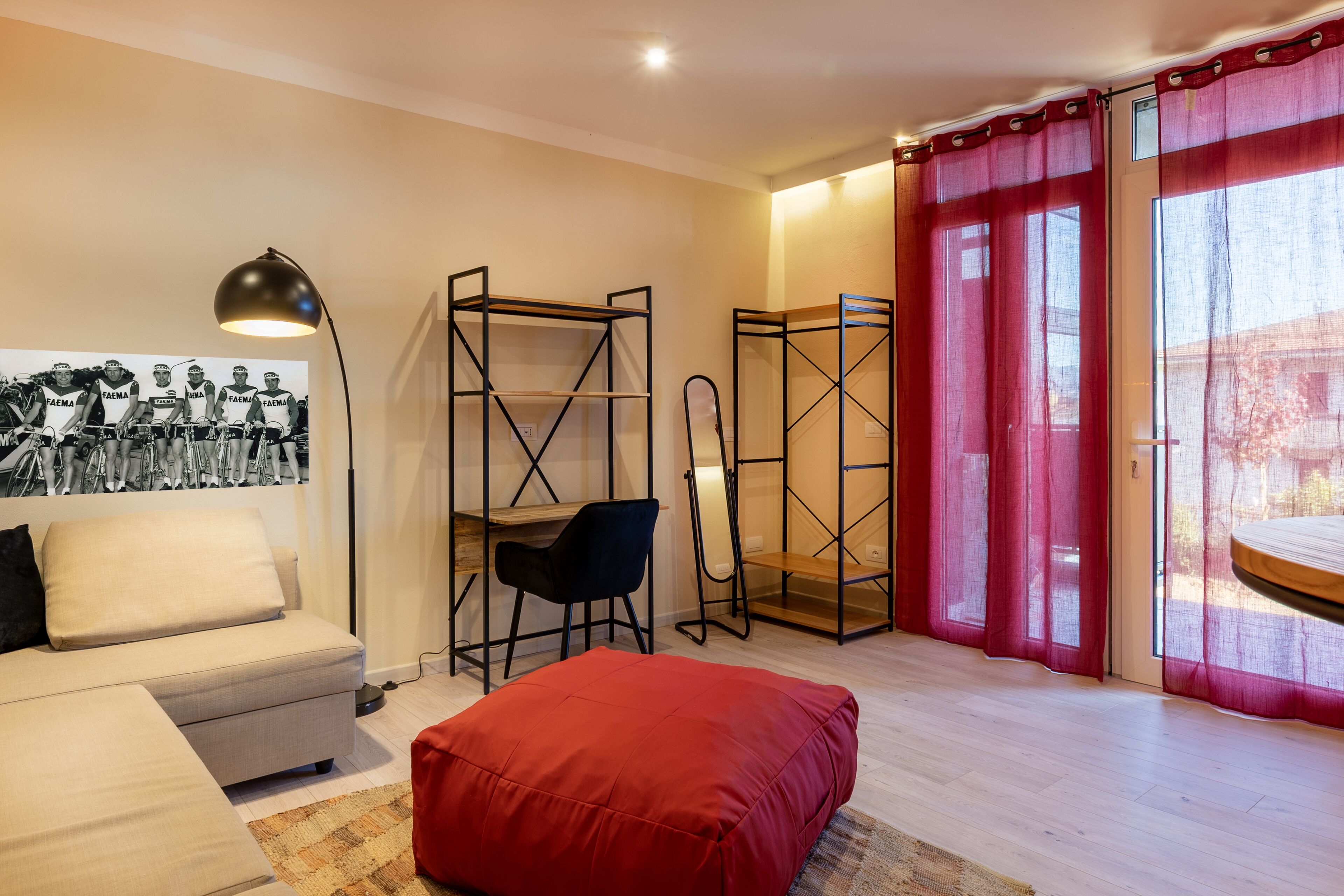 Une pièce moderne comprenant un canapé, un pouf rouge, un bureau avec une chaise et une grande fenêtre ornée de rideaux rouges.