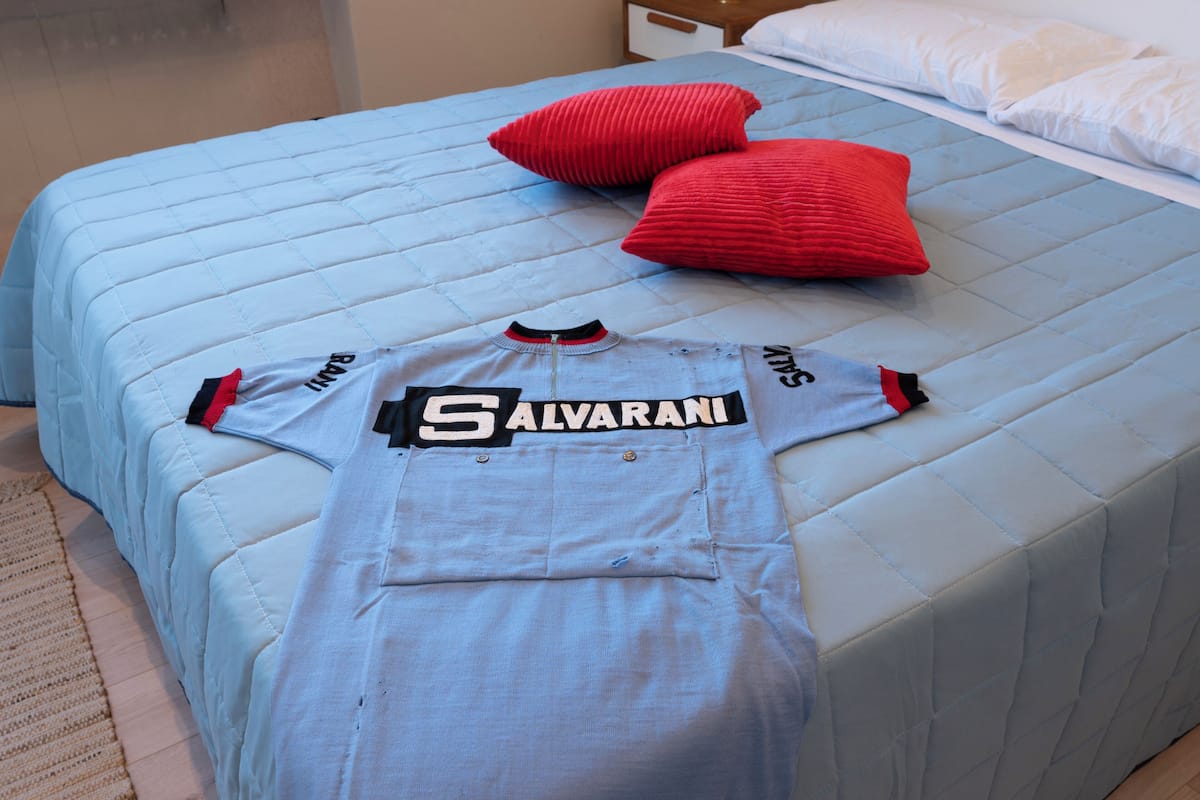 A bed with a blue quilted cover, two red pillows, and a light blue sports jersey with "SALVARANI" text on it.