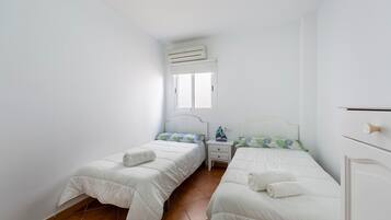 Un dormitorio con dos camas, una ventana, un equipo de aire acondicionado y una mesita de noche con una lámpara.