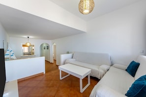 Un salon moderne avec un canapé blanc, une table basse blanche, un bureau blanc et un luminaire suspendu.