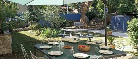 Een terras met een tafel voor vier personen, omringd door metalen stoelen, onder een grote parasol.