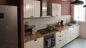 Une cuisine moderne avec des meubles blancs, un réfrigérateur en acier inoxydable, un plan de travail en bois et un sol à motifs.
