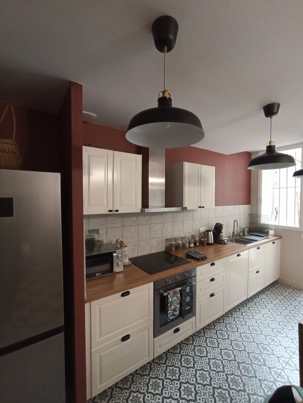 A modern kitchen with white cabinets, a stainless steel refrigerator, a wooden countertop, and a patterned floor.