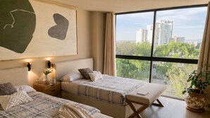 A modern bedroom with two beds, a large window, and a view of buildings. - CityView 2 BedRoom / Daily cleaning (Guadalajara)