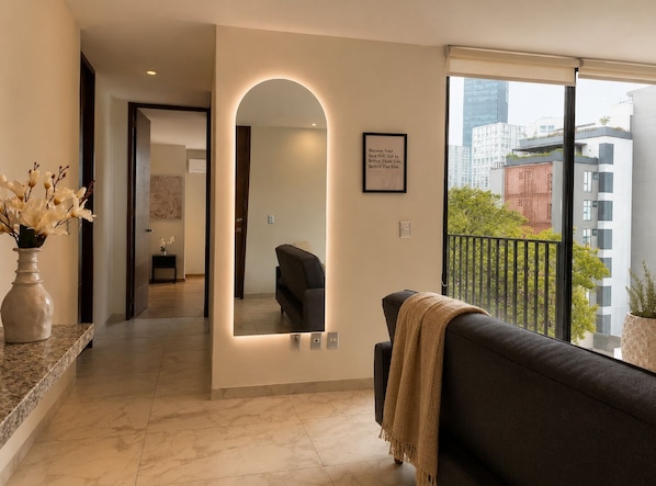 A modern living room with a sofa, a mirror, and a vase of flowers.
