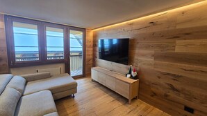 Un salon doté d’un grand téléviseur, de murs recouverts de lambris en bois, d’un canapé et offrant une vue par une fenêtre.