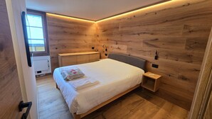Une chambre avec un lambris en bois, un lit, une table de chevet, une commode et une fenêtre.