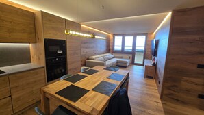 Une cuisine moderne dotée d’appareils électroménagers intégrés, un coin repas avec une table en bois et un espace détente avec un canapé.