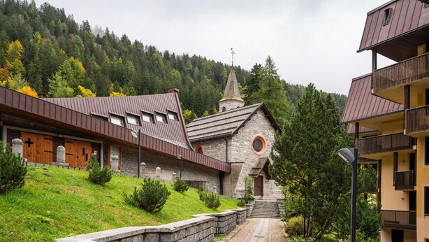 Un bâtiment en pierre surmonté d’un clocher d’église, avec un mur en pierre et un chemin pavé menant à l’entrée.