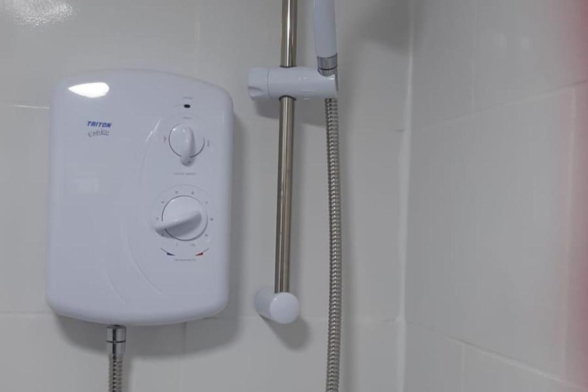 A white TRITON shower unit with two control knobs and a flexible hose.