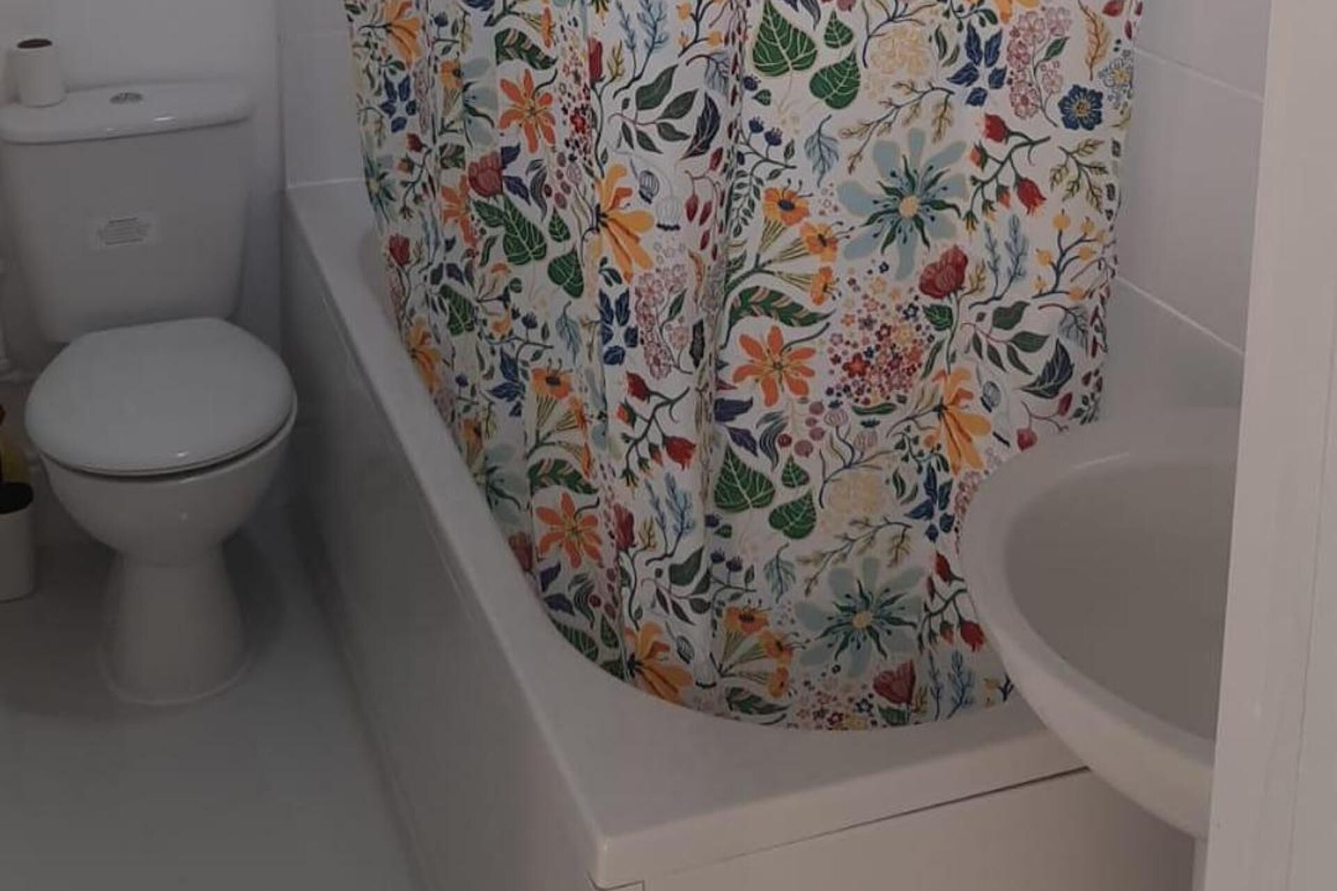 A bathroom with a toilet, a bathtub with floral shower curtains, and a white sink.