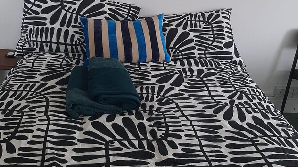 A bed with a black and white leaf pattern, a striped pillow, and a folded blanket.