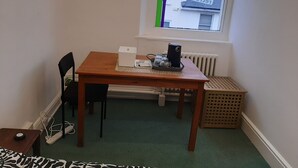 A small room with a wooden table, a chair, a radiator, and a window with a view of buildings outside.