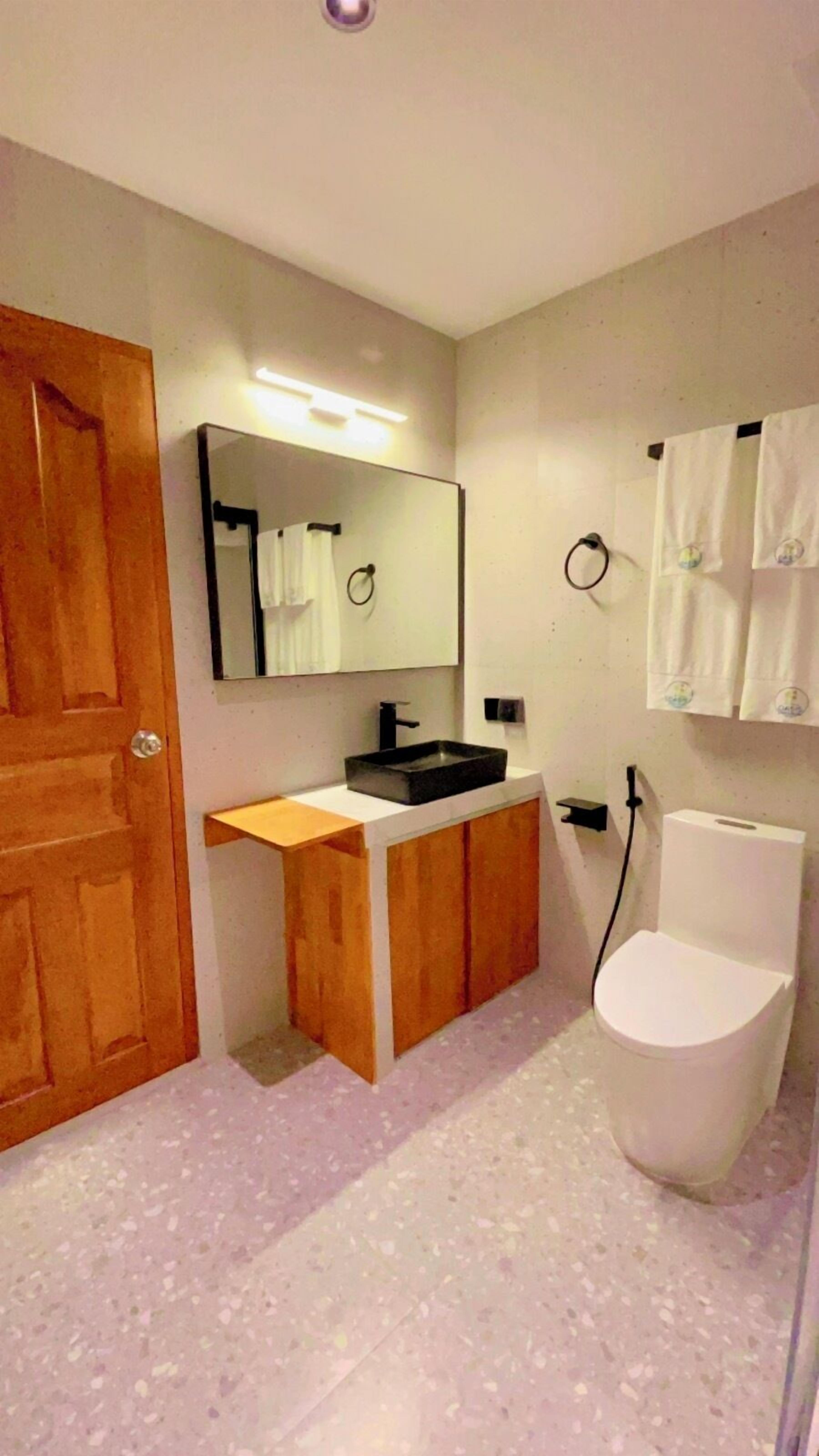 A bathroom with a wooden door, a sink with a mirror, a toilet, and a towel rack.
